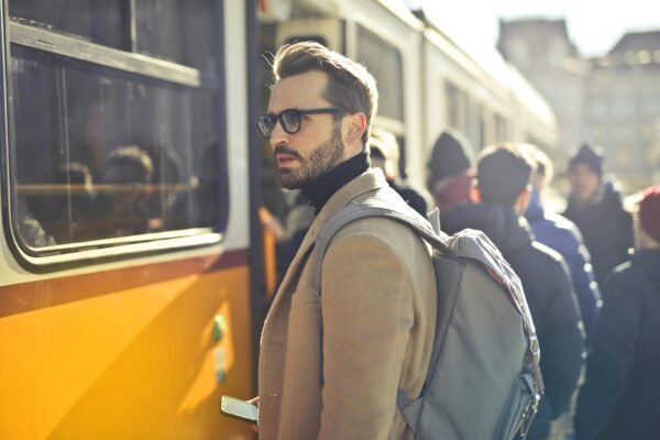 Mercado de estética masculina é promissor para investir em 2025 A stylish man with a backpack boards a tram in bustling Budapest, Hungary, during the day.